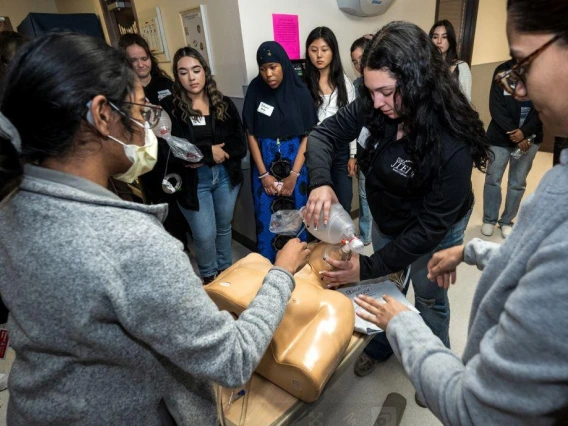 A group of women gathered around a mannequin, engaged in discussion and examining a medical situation.