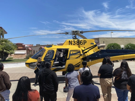 A group of individuals gathered around a helicopter, engaged in conversation and observation.