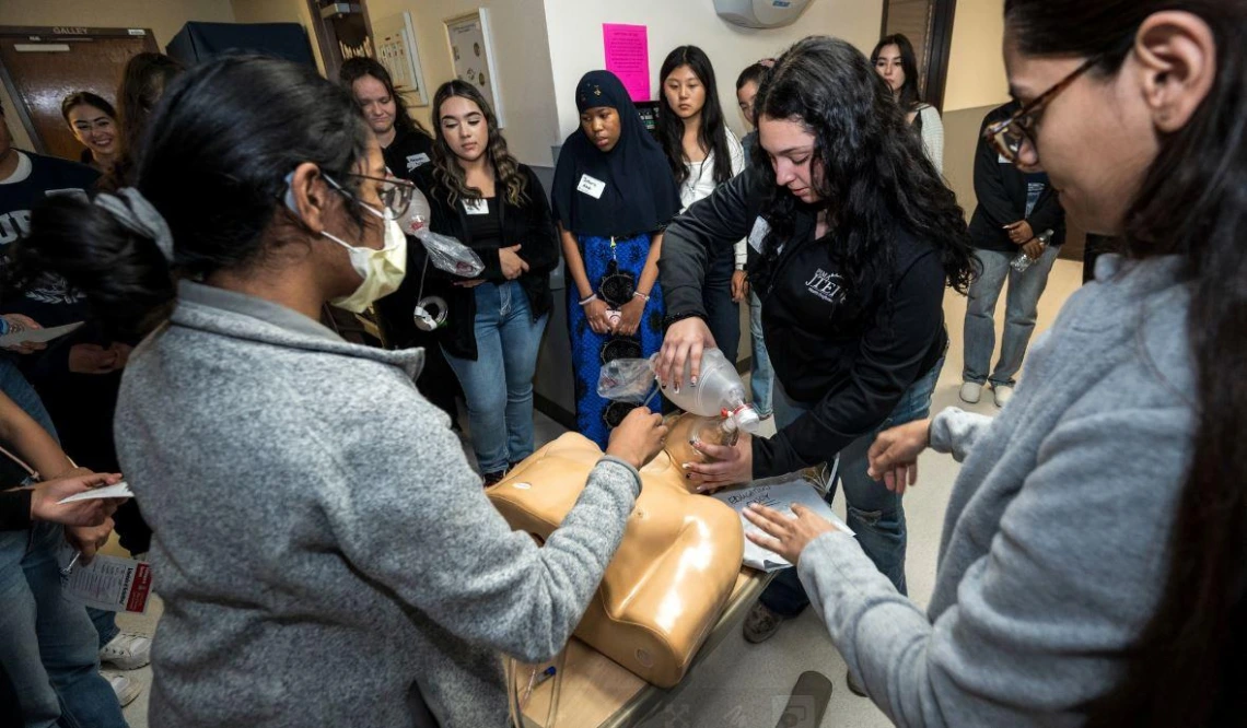 A group of women gathered around a mannequin, engaged in discussion and examining a medical situation.